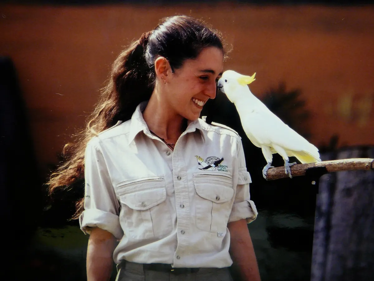 Cassie Malina calmly working hands-on with a large macaw perched on her hand